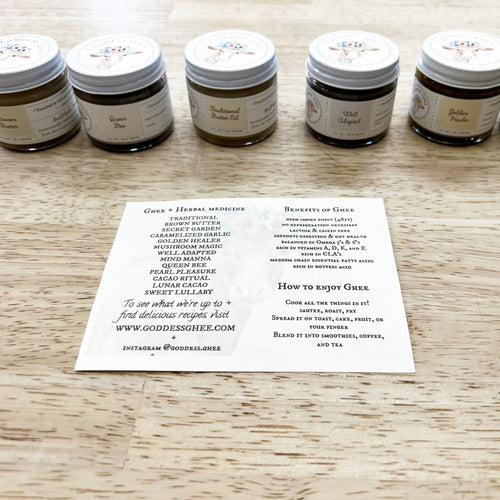 Image of 5 2oz glass jars with a variety of colored ghee (clarified butter) in background with a postcard size paper featuring the names of each ghee blend in the foreground on a light butcher block tabletop.